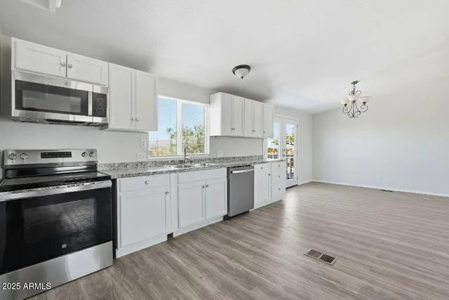 a kitchen with stainless steel appliances granite countertop a stove top oven a sink dishwasher and a microwave oven on the wooden floor