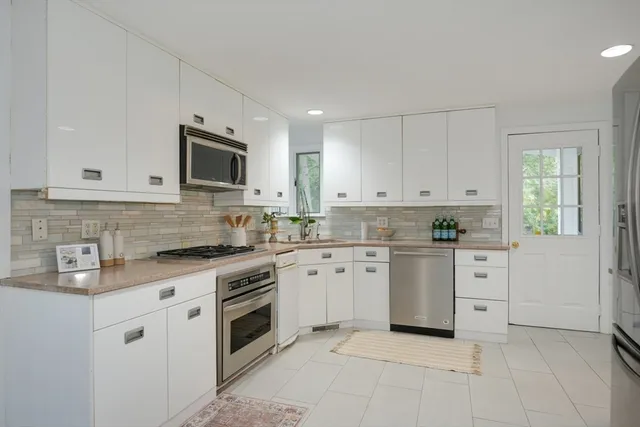 a kitchen with white cabinets appliances a sink and a window