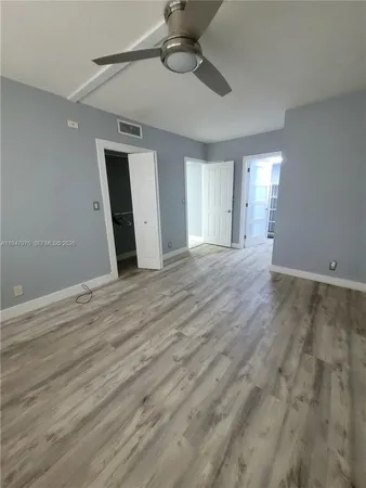 a view of an empty room with wooden floor and fan