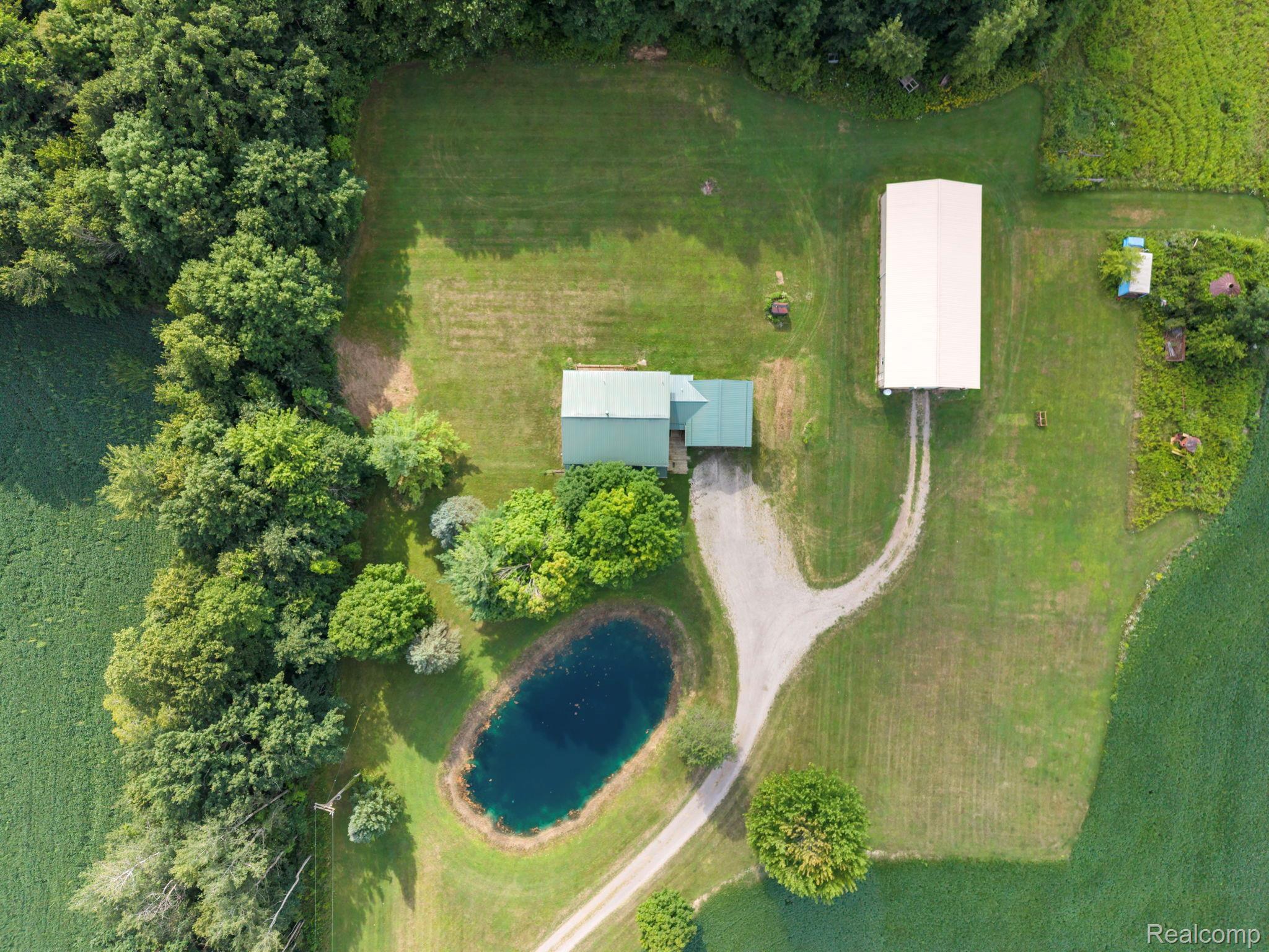 76565 McFadden Road Armada, MI 48005 - Photo 85 of 95 Expansive grounds featuring a main residence with a green metal roof, a large outbuilding, a gravel driveway, and a pond