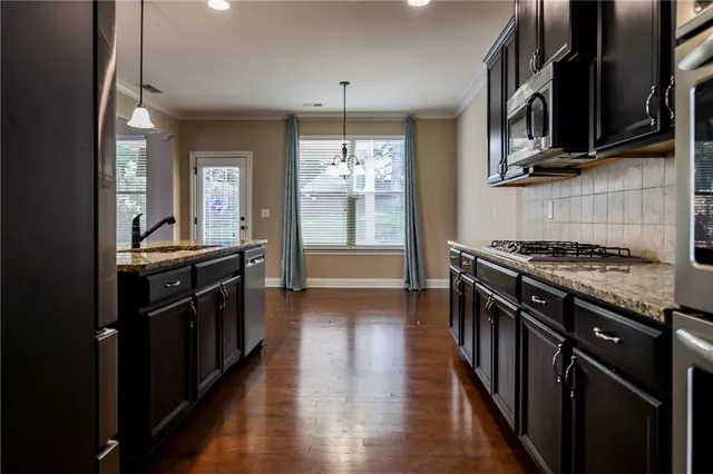 a kitchen with stainless steel appliances granite countertop a stove top oven a sink dishwasher a refrigerator and a cabinets with wooden floor