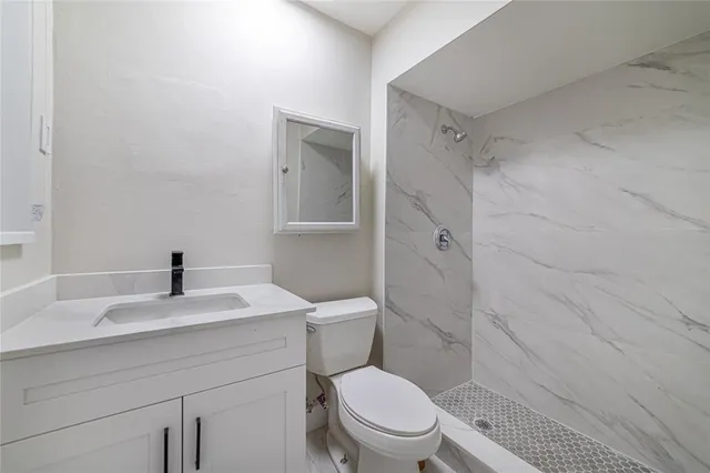 a spacious bathroom with a granite countertop sink a toilet a mirror and shower