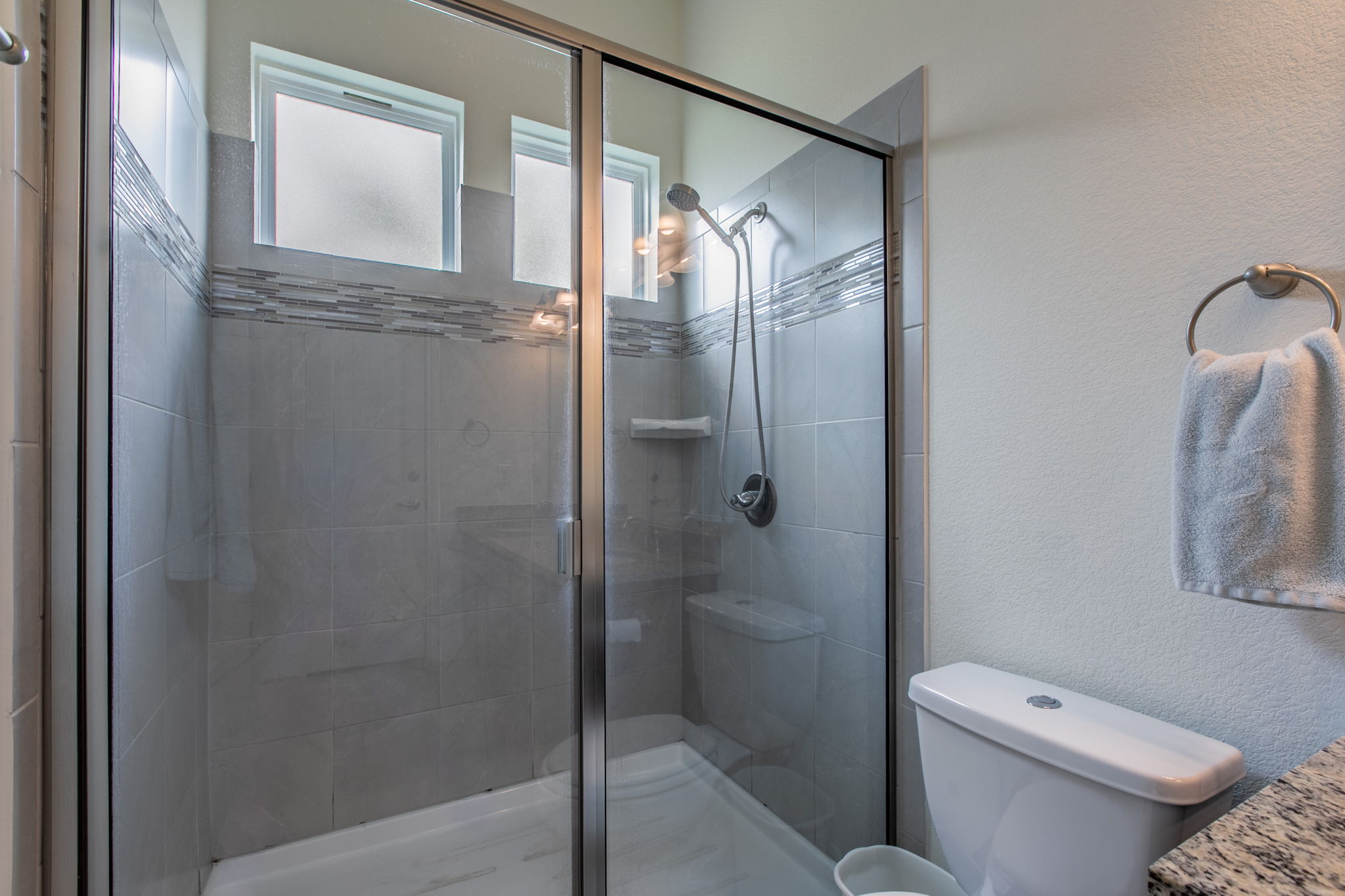 231 Simon Kyle, TX 78640 - Photo 16 of 29 Glass-enclosed shower featuring light gray tile walls with a decorative mosaic accent band