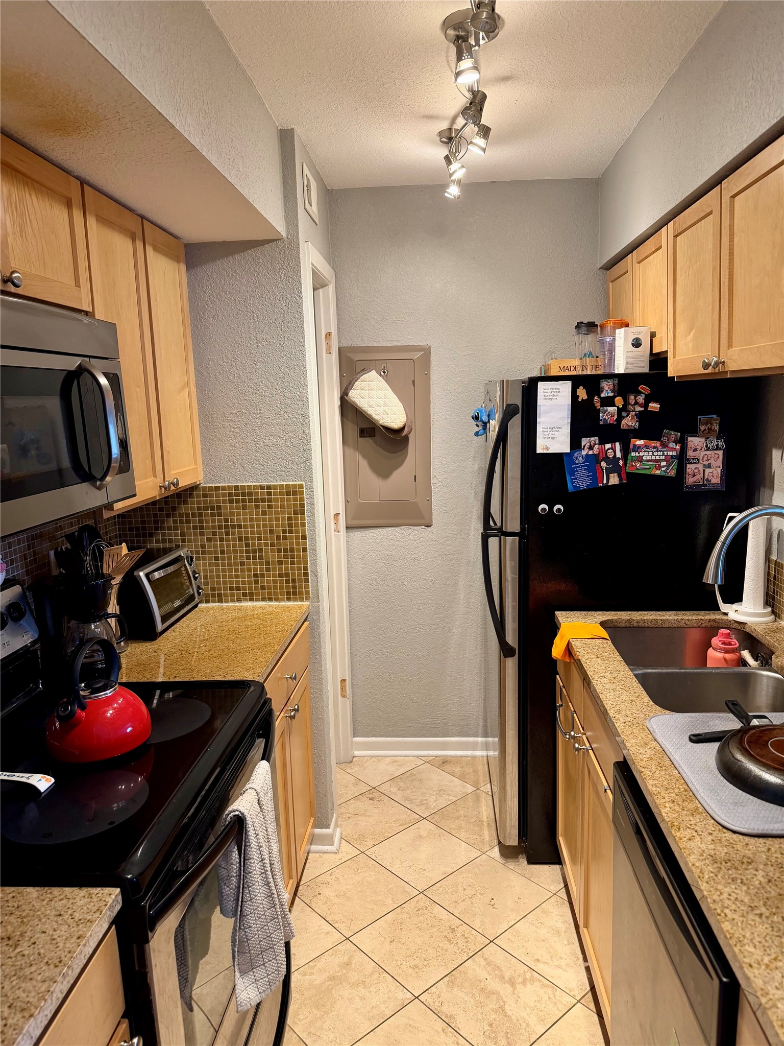 3204 Menchaca Road, Unit 204 Austin, TX 78704 - Photo 8 of 18 Kitchen with stainless steel appliances, a textured wall, light wood finish cabinetry, light stone countertops, and a textured ceiling