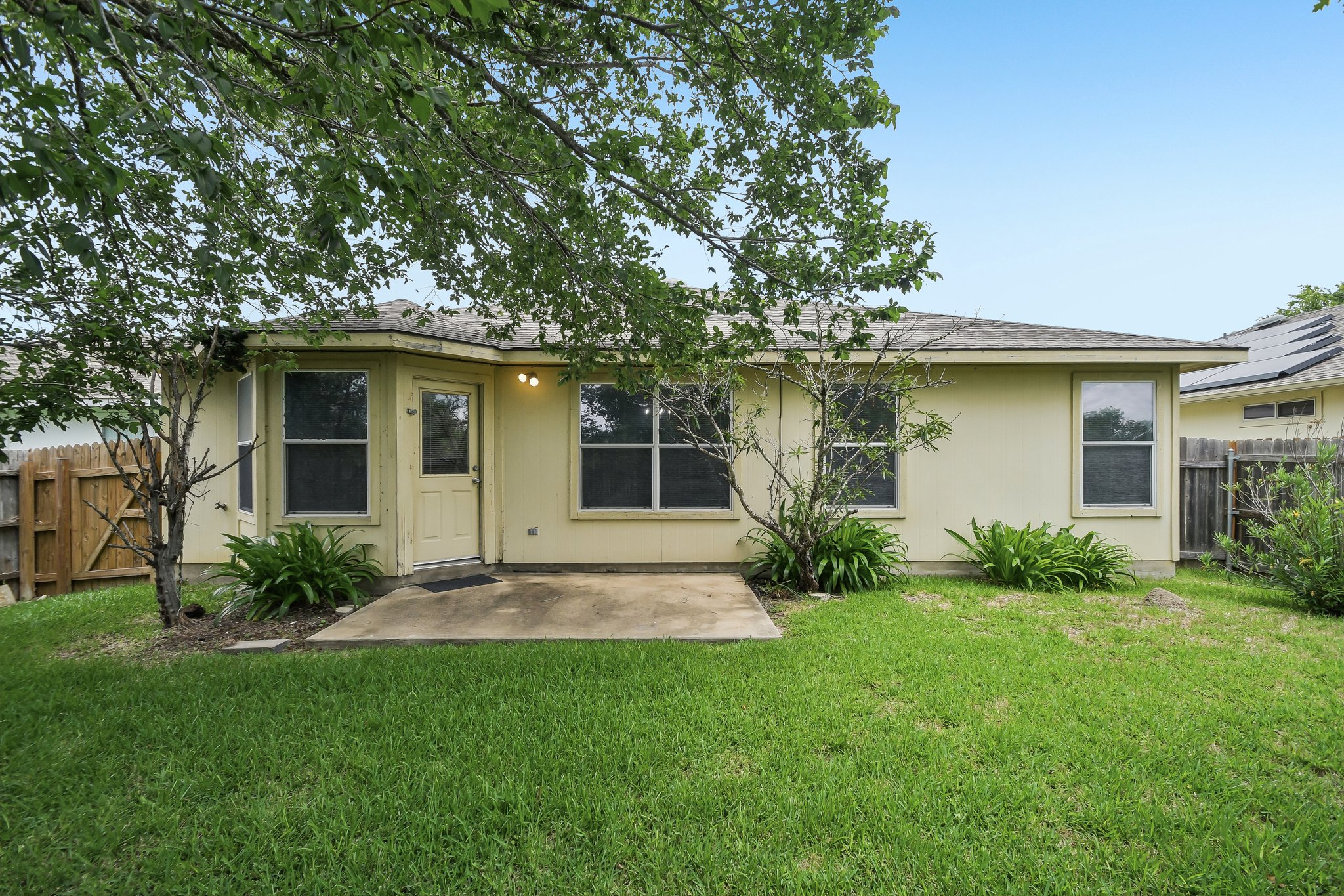 610 Lavaca Loop Elgin, TX 78621 - Photo 34 of 37 A well-maintained lawn stretches to a practical patio and inviting rear entry, bordered by mature trees and privacy fencing.