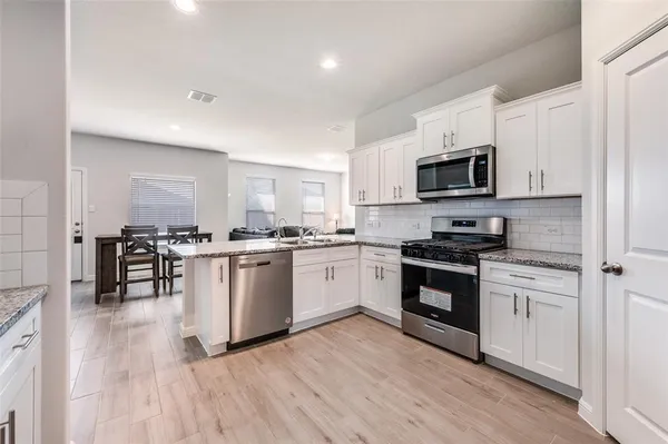 a kitchen with granite countertop a stove top oven a sink dishwasher a dining table and chairs with wooden floor
