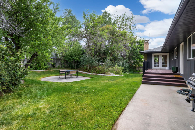 4150 Dover Lane Provo, UT 84604 - Photo 38 of 44 Expansive backyard featuring a manicured lawn, a circular concrete patio, mature trees, a multi-level wood deck, and French doors leading into the property