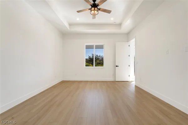 an empty room with wooden floor chandelier fan and windows
