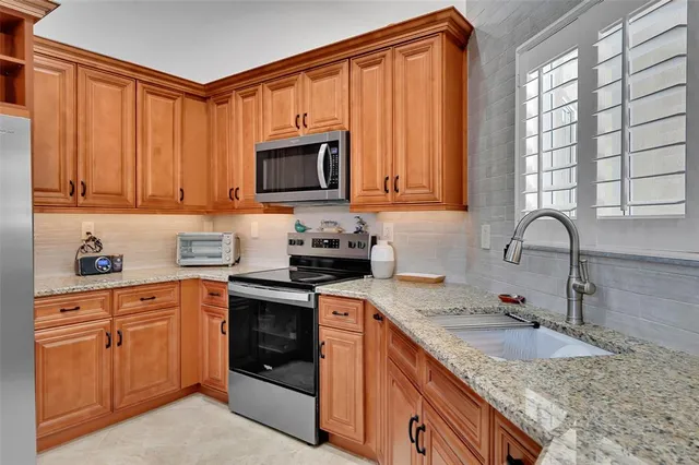 a kitchen with granite countertop a sink stainless steel appliances wooden cabinets and a window