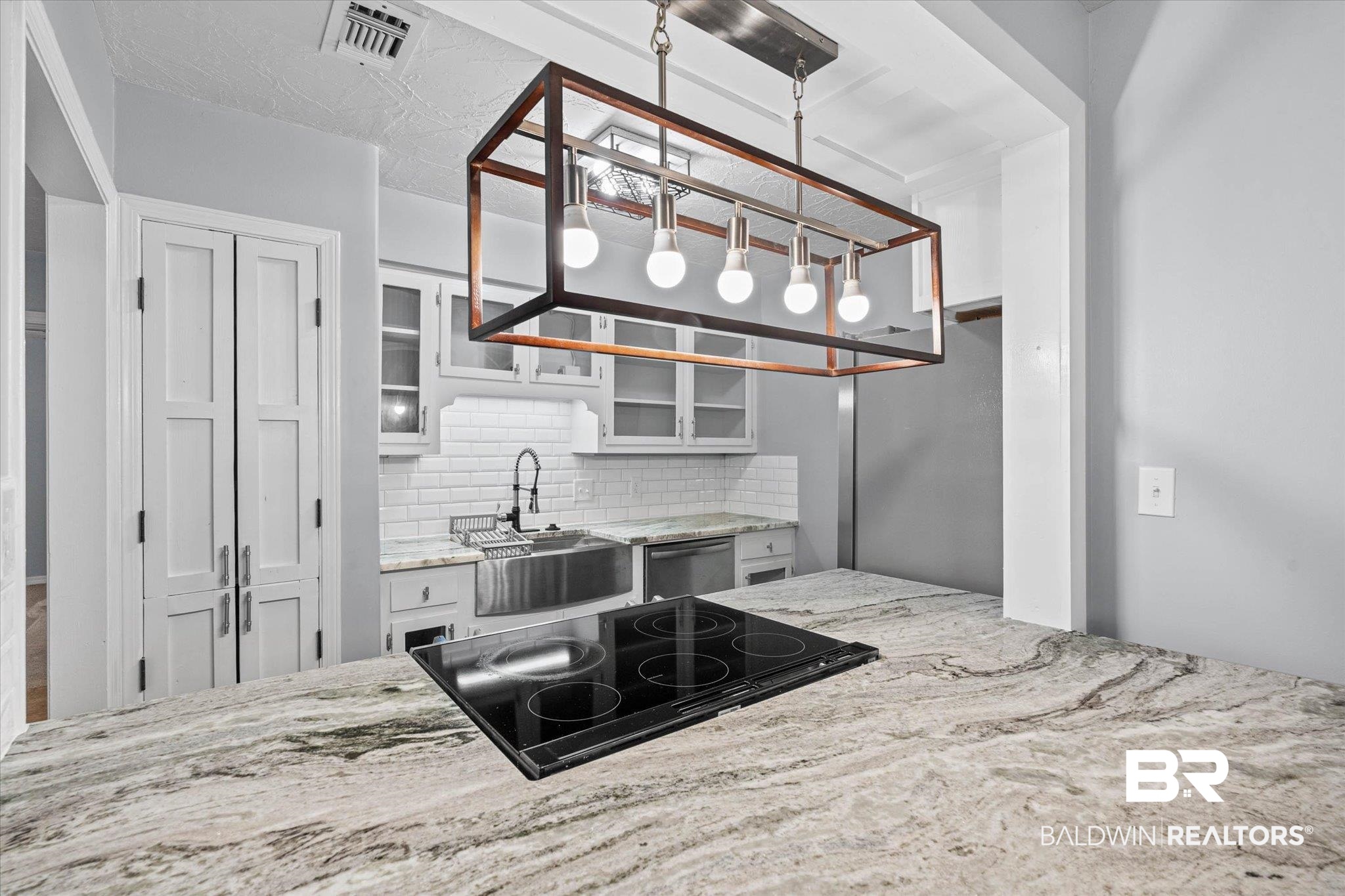 500 Grant Street, Unit C210 Daphne, AL 36526 - Photo 10 of 26 Kitchen featuring a large island with a built-in cooktop, a stainless steel farmhouse sink, white subway tile backsplash, and light-colored cabinetry