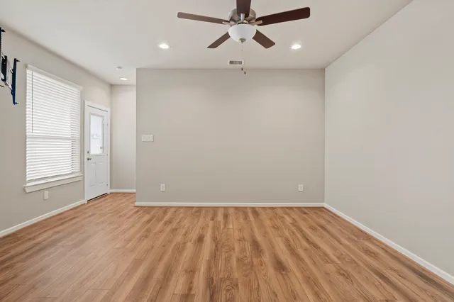 an empty room with wooden floor ceiling fan and windows