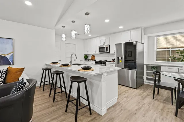 a kitchen with stainless steel appliances granite countertop a stove a refrigerator a kitchen island a dining table and chairs with wooden floor