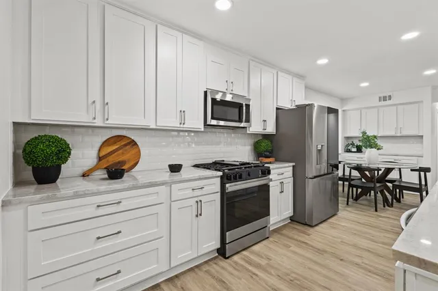 a kitchen with stainless steel appliances granite countertop a stove a refrigerator a microwave oven with white cabinets and wooden floor