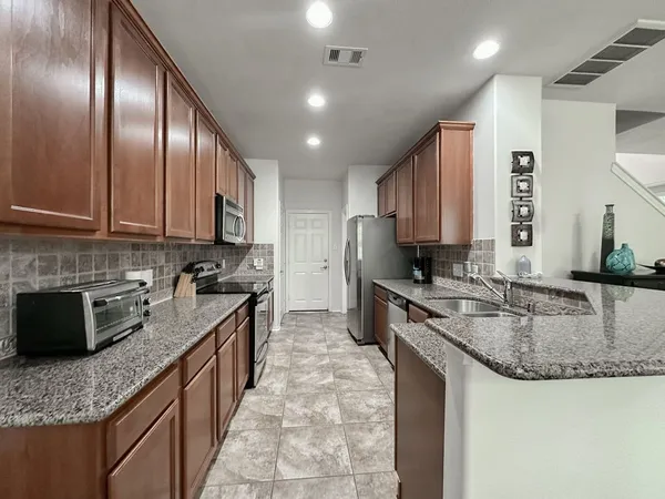 a kitchen with granite countertop stainless steel appliances a sink dishwasher a stove top oven a refrigerator with wooden cabinets and floor