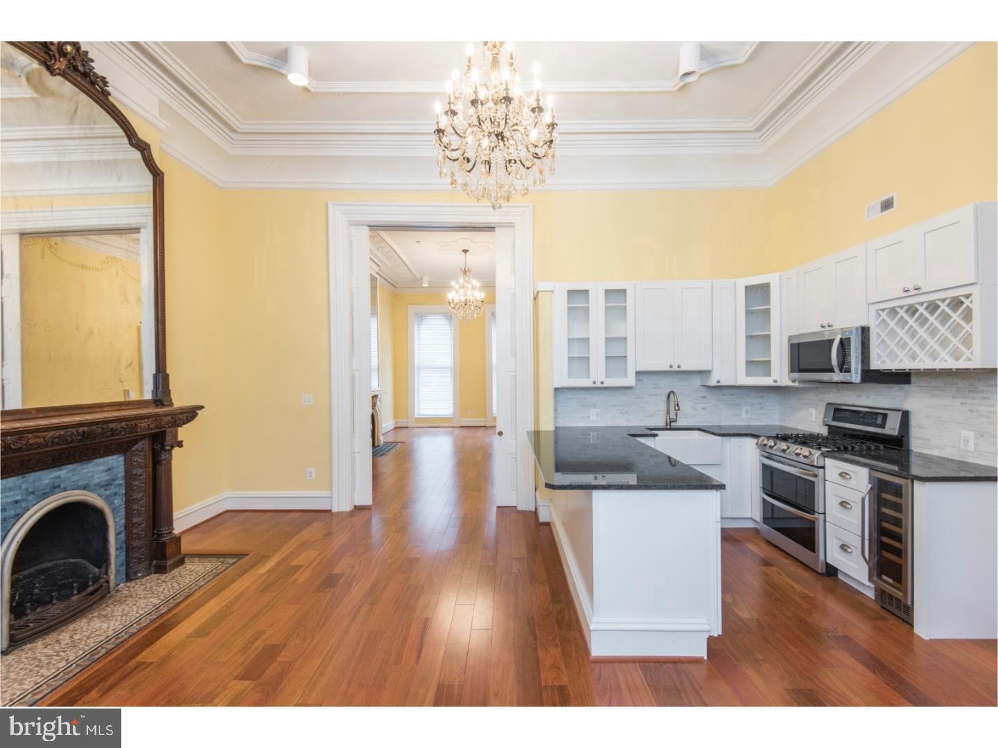 2129 Walnut Street, Unit 1 Philadelphia, PA 19103 - Photo 2 of 7 a open kitchen with granite countertop a stove top oven a sink dishwasher and a fireplace with wooden floor