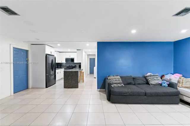 a living room with stainless steel appliances kitchen island granite countertop a refrigerator and a sink
