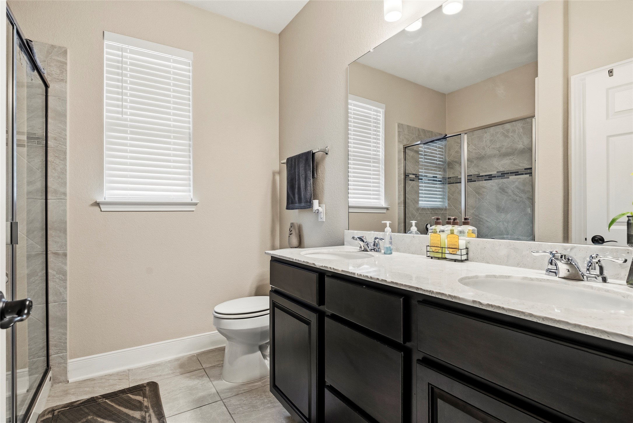 105 West Point Way Elgin, TX 78621 - Photo 25 of 27 Bathroom featuring a double vanity with an integrated countertop, built-in cabinetry, an enclosed glass shower, and a privacy window with blinds