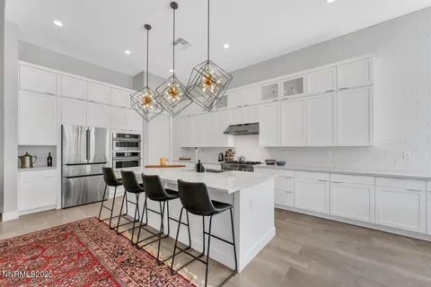 a kitchen with stainless steel appliances granite countertop a sink a stove a refrigerator cabinets and chairs