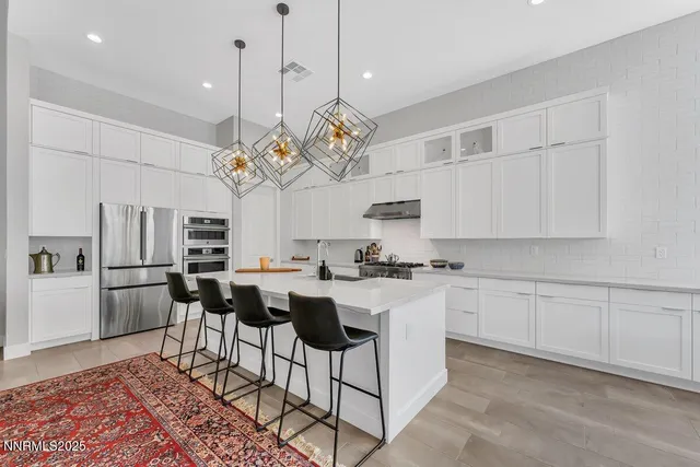 a kitchen with stainless steel appliances granite countertop a sink a stove a refrigerator cabinets and chairs