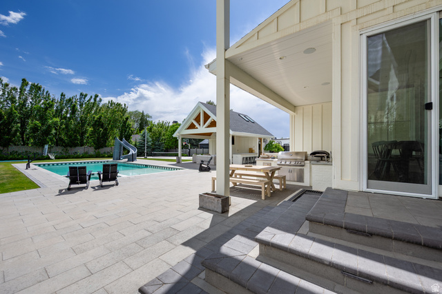 630 East Center Street Alpine, UT 84004 - Photo 104 of 115 Expansive outdoor living area featuring a rectangular pool with a waterslide, a large paved patio, a covered outdoor kitchen with built-in grill, a separate covered structure, and mature perimeter trees