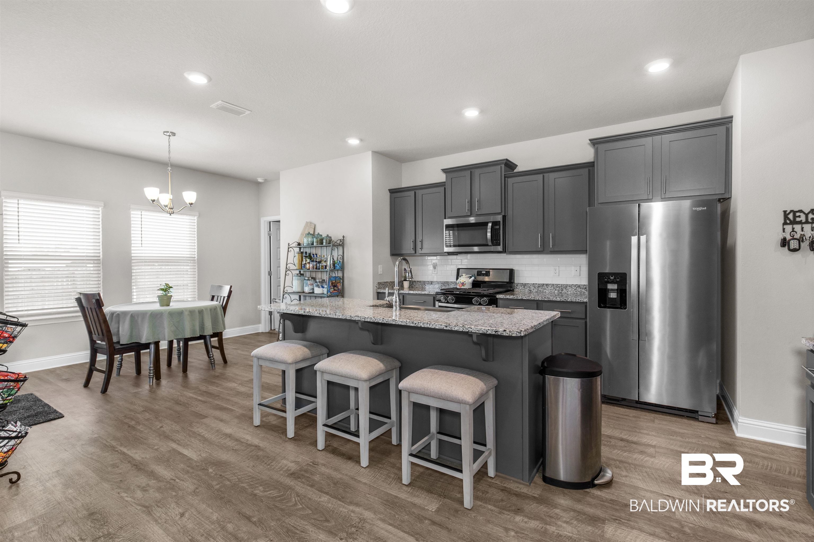 2345 Laurel Street Semmes, AL 36575 - Photo 8 of 31 Kitchen with appliances with stainless steel finishes, an island with sink, a breakfast bar area, wood finished floors, and light stone counters