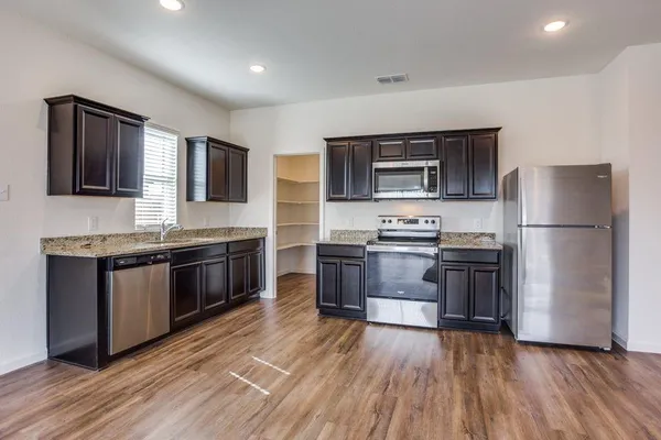 a kitchen with granite countertop wooden floors stainless steel appliances and sink