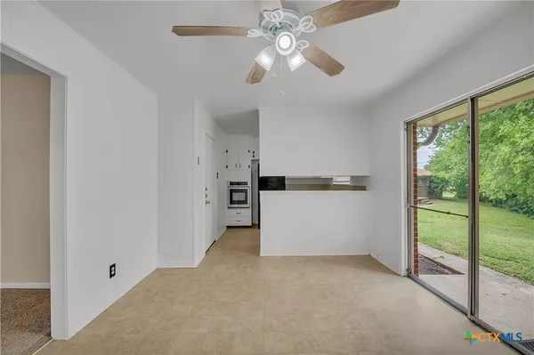 an empty room with chandelier fan and windows