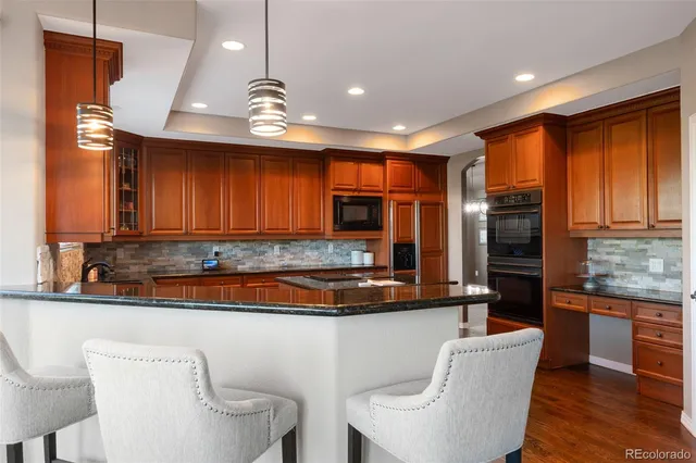 a kitchen with stainless steel appliances granite countertop a refrigerator a sink dishwasher a stove and a dining table with wooden floor