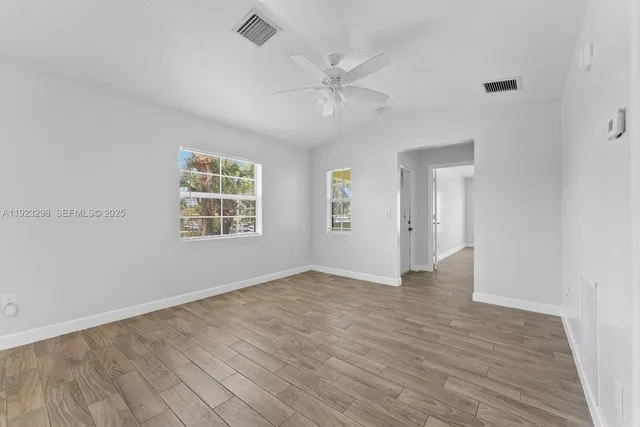 an empty room with wooden floor chandelier fan and windows