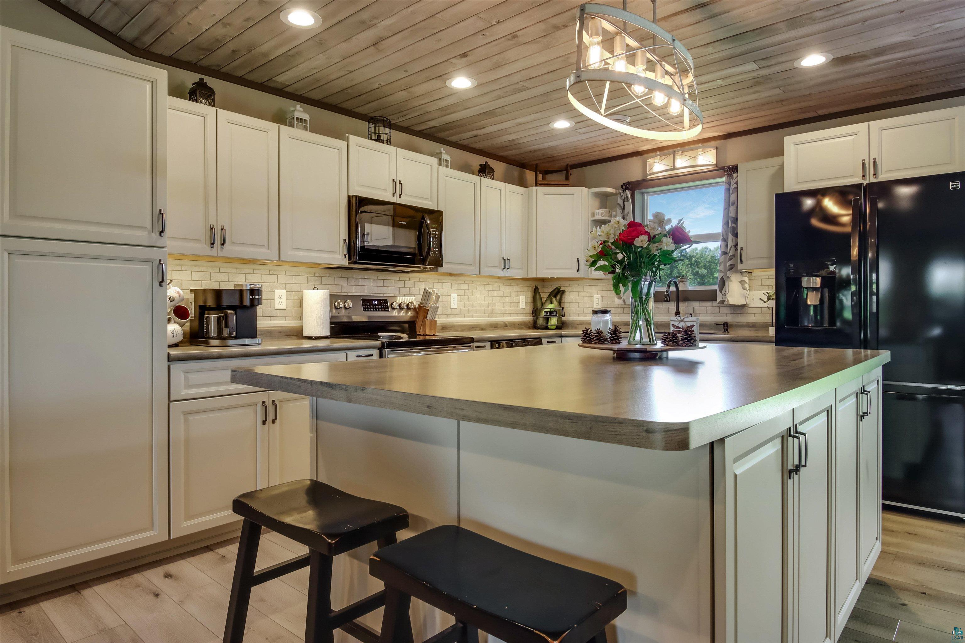 N3685 Fenander Road Spooner, WI 54801 - Photo 18 of 38 Kitchen featuring white cabinetry, black appliances, a center island, wooden ceiling, and light hardwood / wood-style floors
