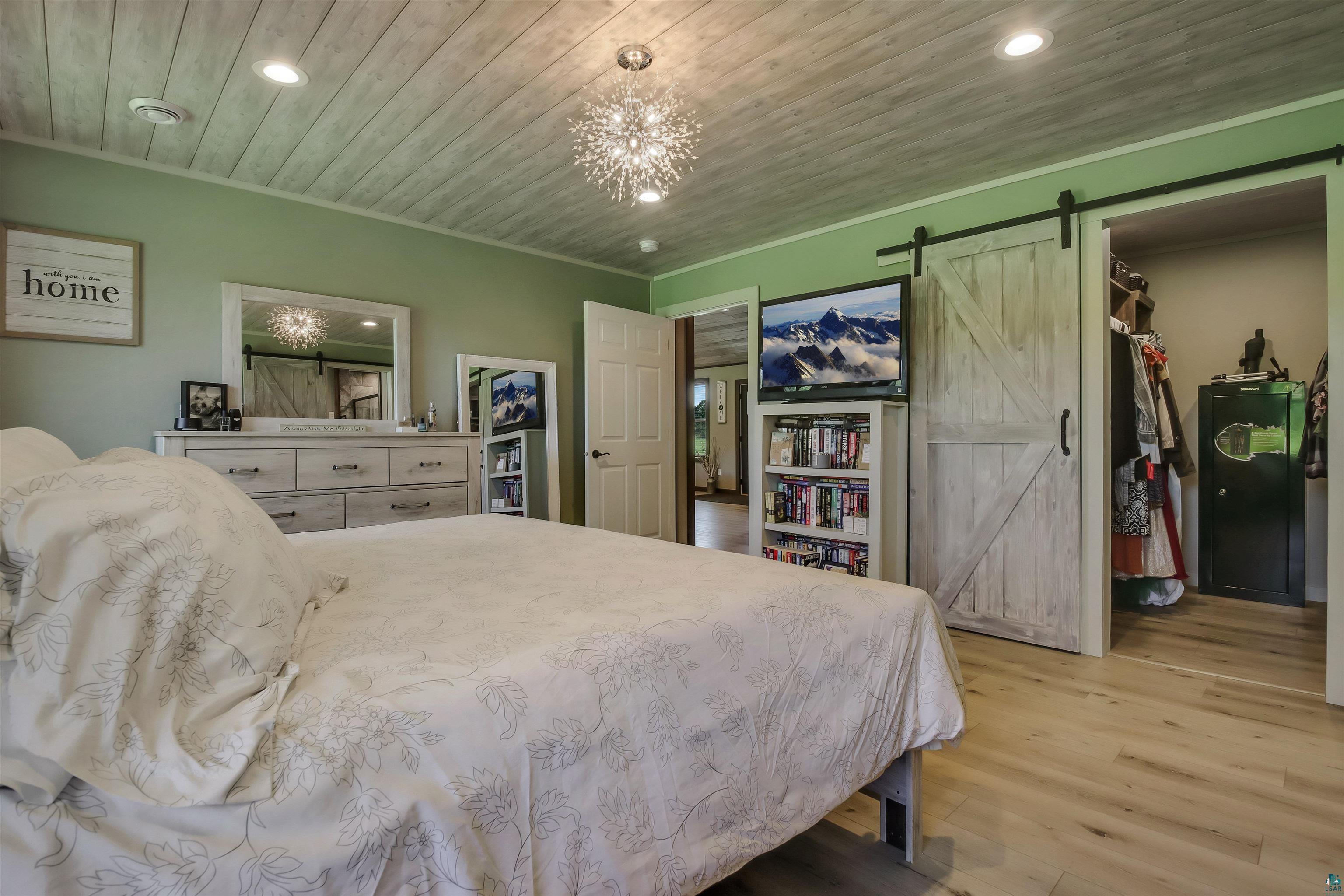 N3685 Fenander Road Spooner, WI 54801 - Photo 26 of 38 Bedroom featuring a walk in closet, a notable chandelier, light hardwood / wood-style floors, wood ceiling, and a barn door