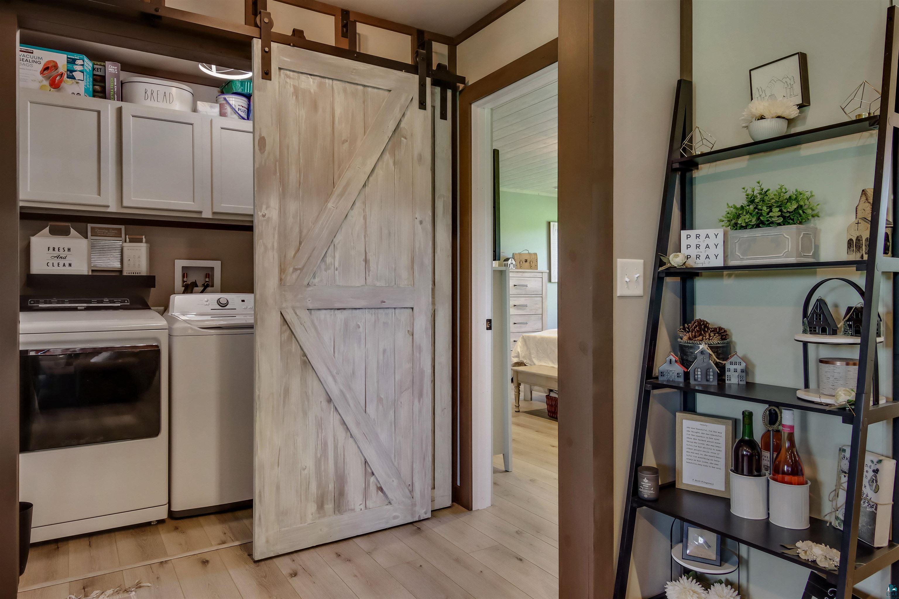 N3685 Fenander Road Spooner, WI 54801 - Photo 33 of 38 Laundry area featuring separate washer and dryer, cabinets, a barn door, and light hardwood / wood-style floors