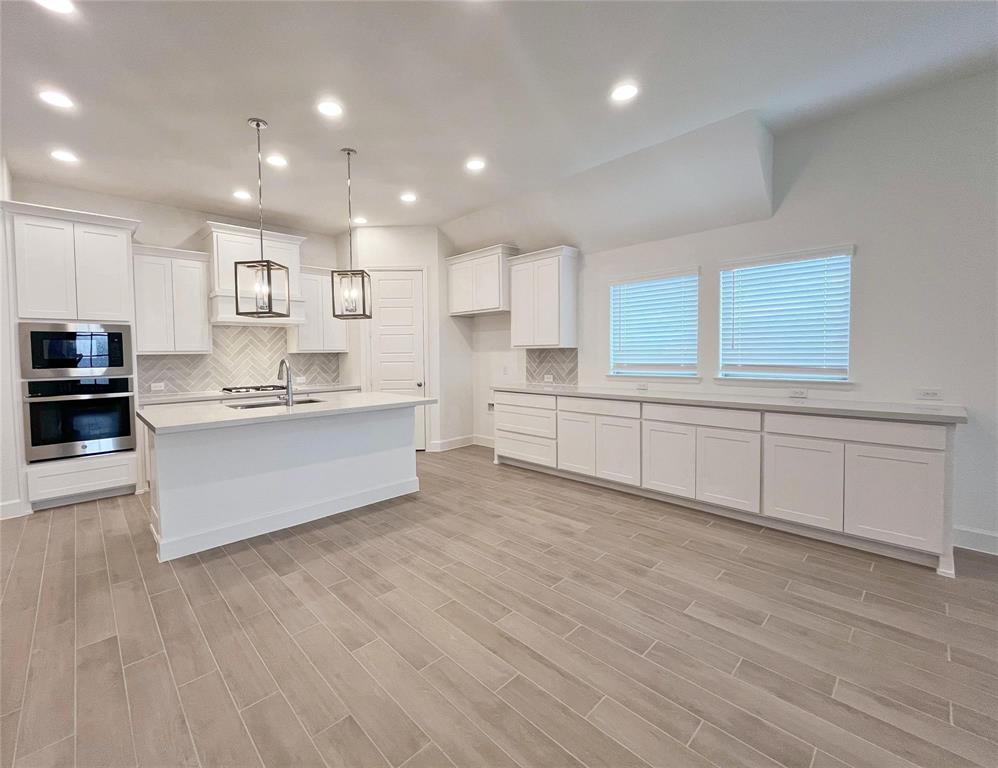 4315 Hudson Street Fate, TX 75087 - Photo 4 of 15 a large white kitchen with kitchen island a sink dishwasher a stove and white cabinets with wooden floor