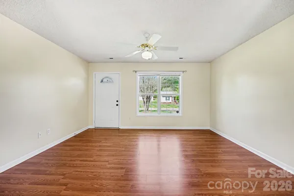 an empty room with wooden floor chandelier fan and windows