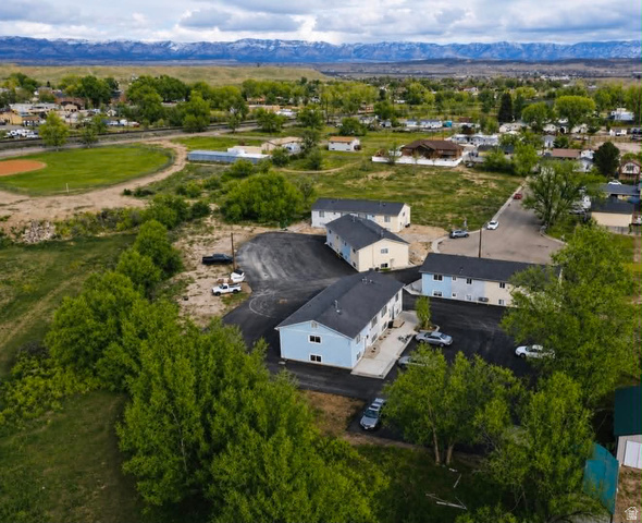 102 East Richelman Lane Wellington, UT 84542 - Photo 4 of 43 Three multi-unit structures with light-toned siding and dark roofs, surrounded by mature trees and paved parking areas