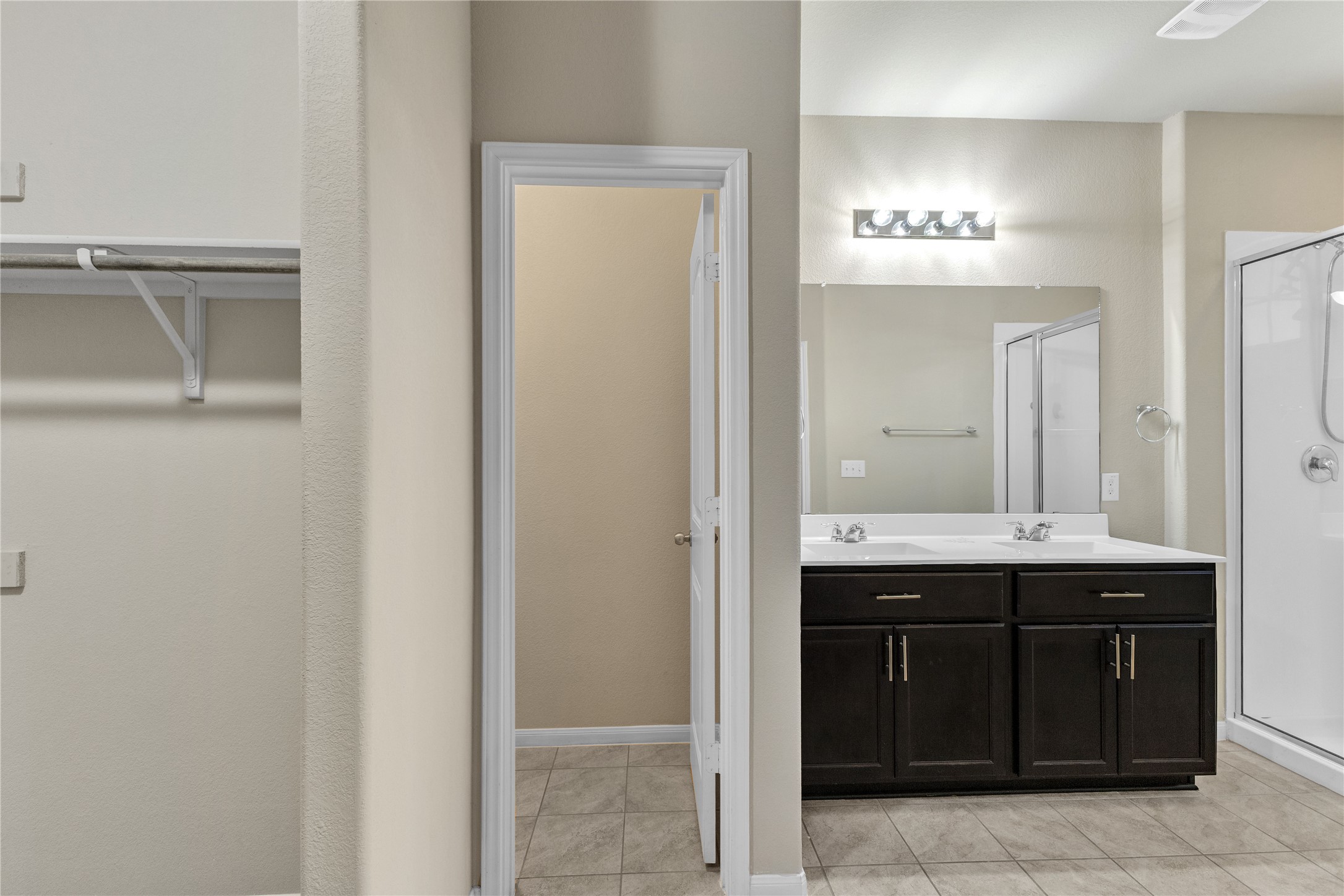 2880 Donnell Drive, Unit 2003 Round Rock, TX 78664 - Photo 26 of 31 Bathroom featuring a dark wood-finish dual vanity with undermount sinks, a mirrored wall with a four-bulb light fixture, a tiled shower with a clear glass enclosure, and tiled flooring