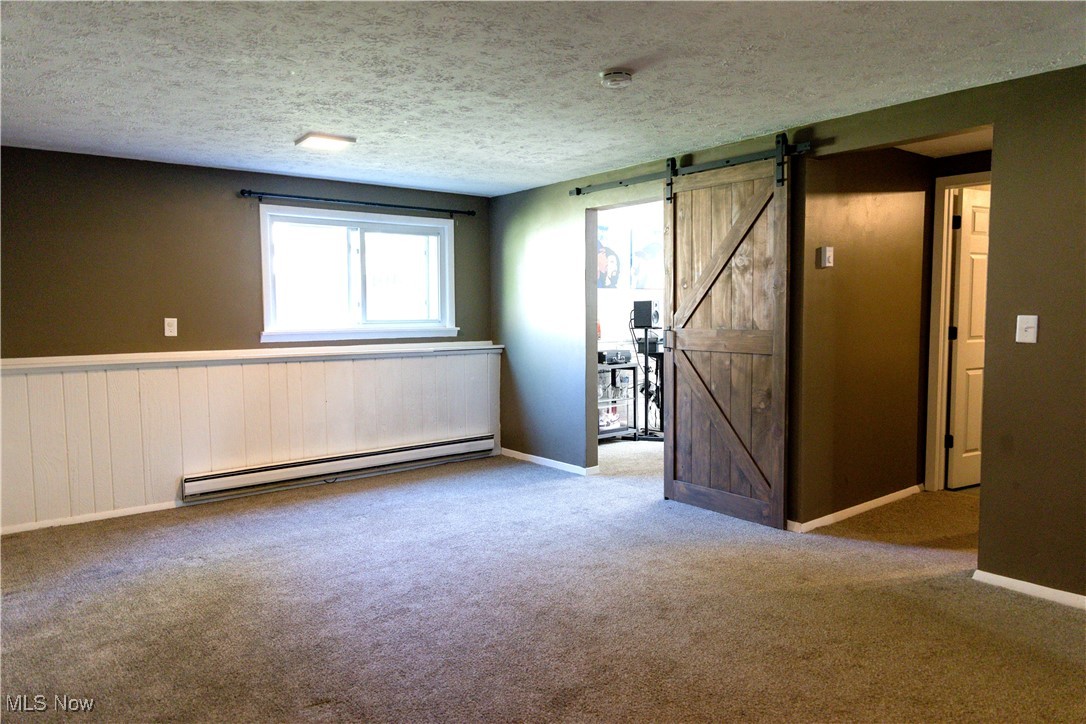 5861 Lee Avenue North Ridgeville, OH 44039 - Photo 15 of 20 Spare room featuring a barn door, a textured ceiling, a baseboard radiator, light carpet, and a wainscoted wall