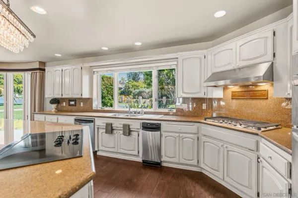 a kitchen with stainless steel appliances granite countertop a stove a sink and white cabinets with wooden floor