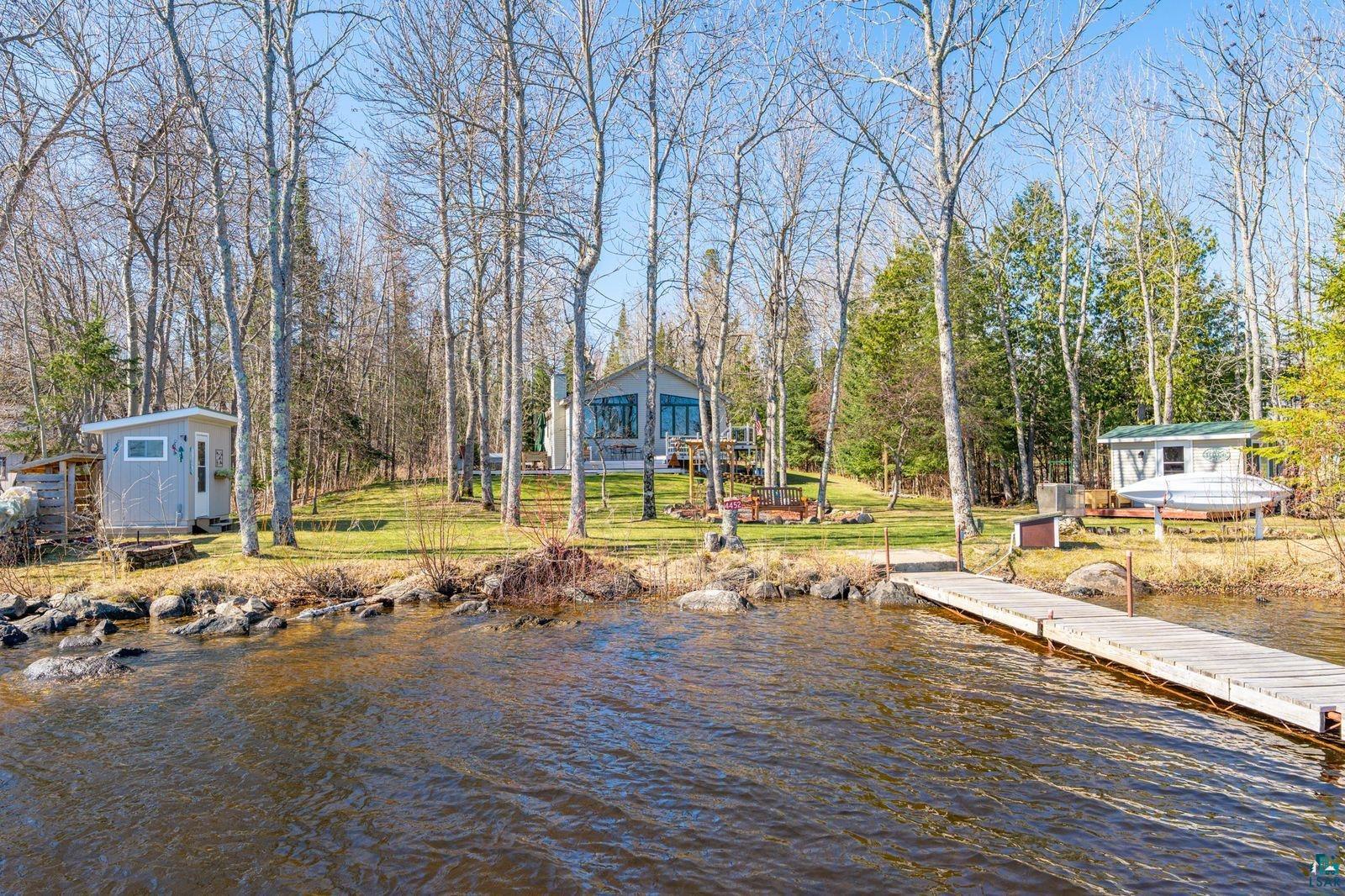 4452 Moccasin Point Road Tower, MN 55790 - Photo 40 of 44 Waterfront property featuring a wooden dock, mature trees, a main residence with large windows, and two additional structures