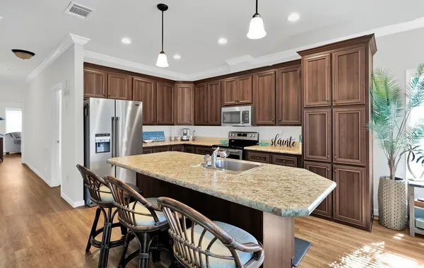 a kitchen with stainless steel appliances granite countertop a kitchen island a stove a refrigerator a sink a dining table and chairs with wooden floor