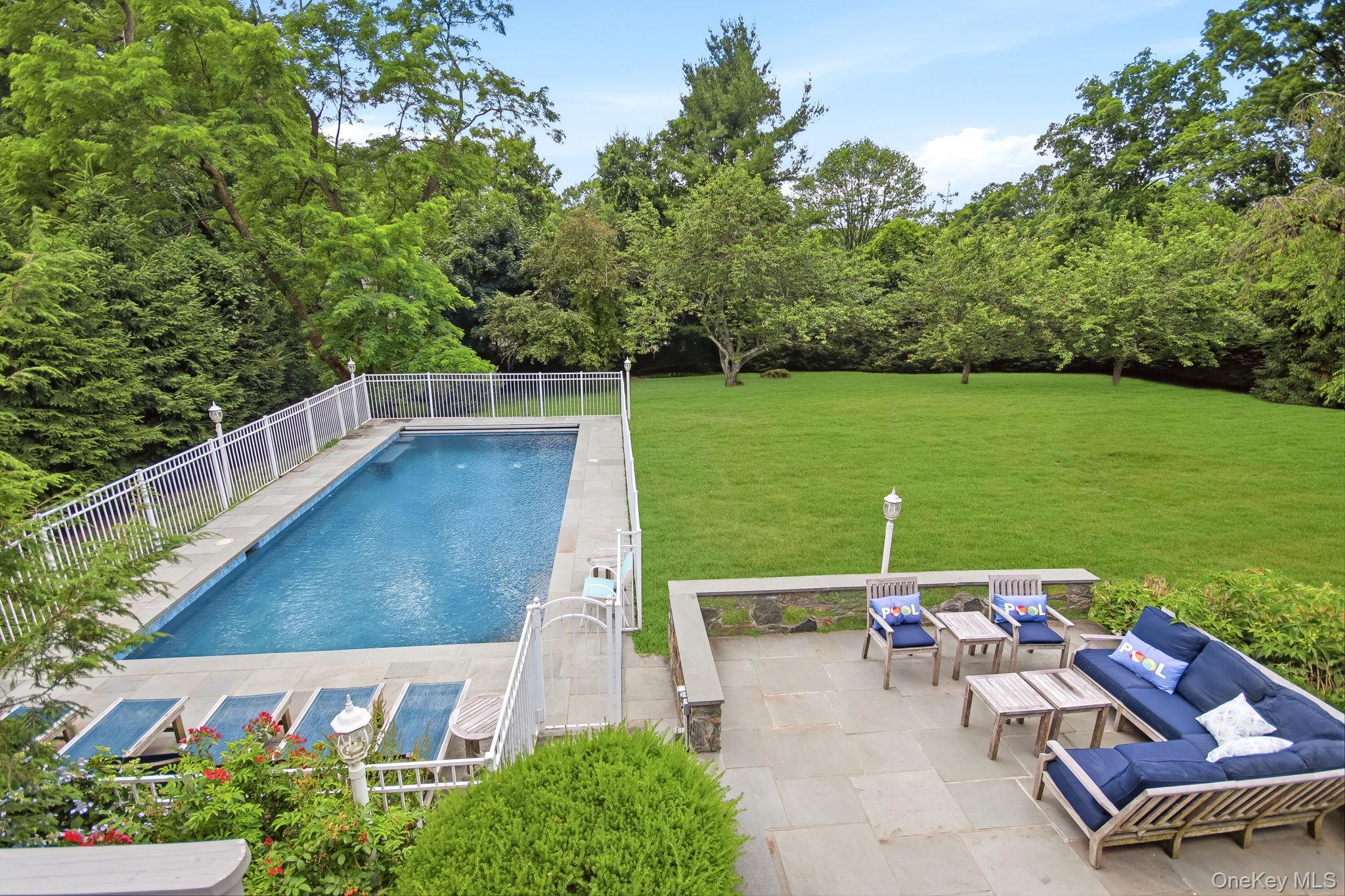 26 Century Ridge Road Purchase, NY 10577 - Photo 39 of 50 Outdoor entertaining space featuring a rectangular swimming pool with safety fencing, a stone patio, and an expansive lawn area