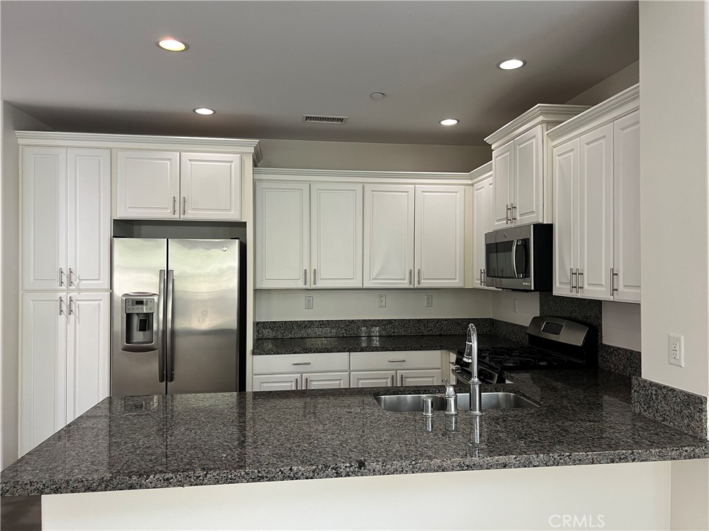 104 Rose Arch Irvine, CA 92620 - Photo 4 of 12 a kitchen with stainless steel appliances granite countertop a stove a sink a microwave a refrigerator and white cabinets with wooden floor