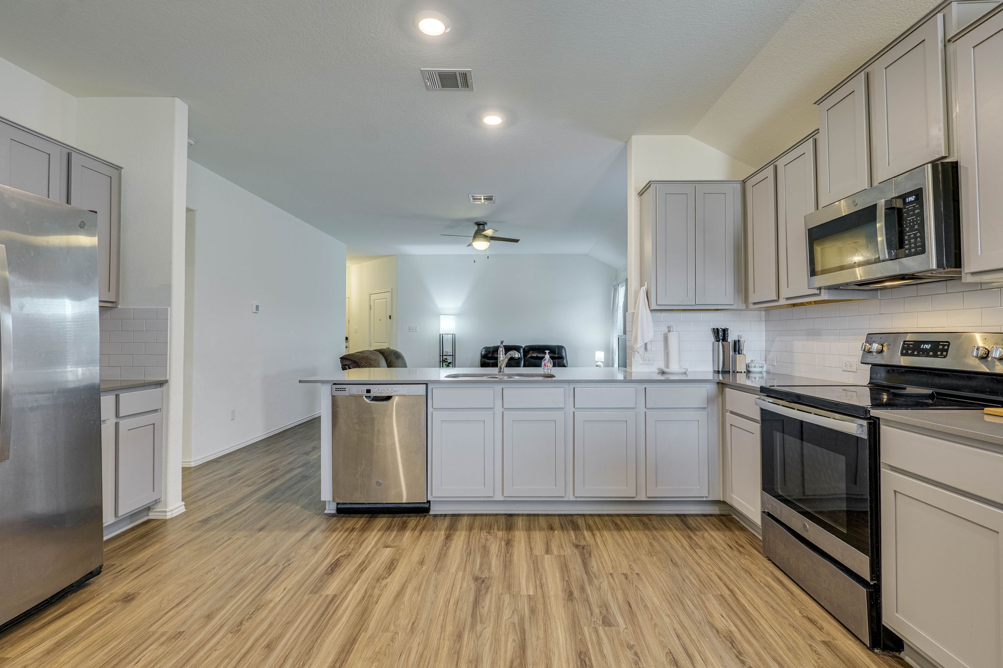 557 Greatest Gift Way Jarrell, TX 76537 - Photo 13 of 39 Kitchen featuring decorative backsplash, stainless steel appliances, lofted ceiling, gray cabinetry, and a peninsula