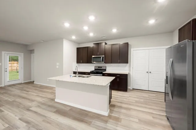 a kitchen with stainless steel appliances kitchen island granite countertop a refrigerator a stove and a sink with wooden floor