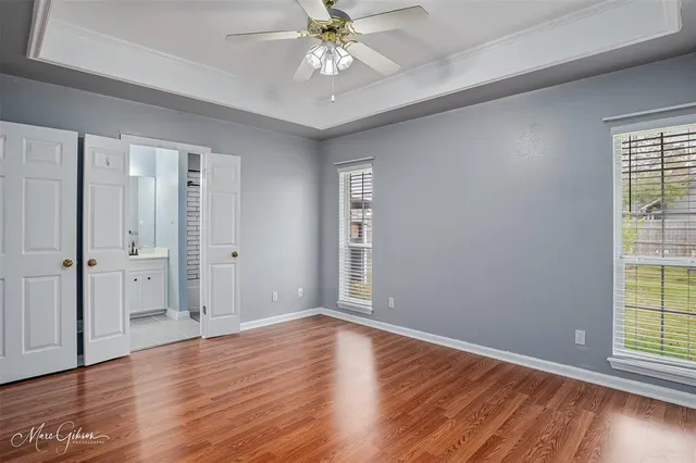 an empty room with wooden floor chandelier fan and windows