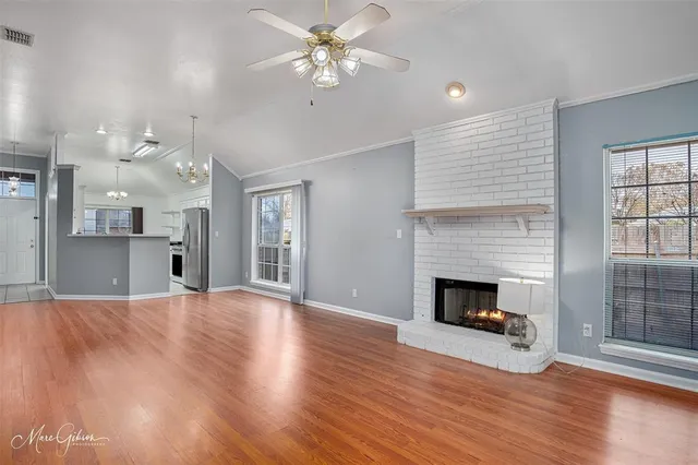 a view of an empty room with wooden floor fireplace and a window