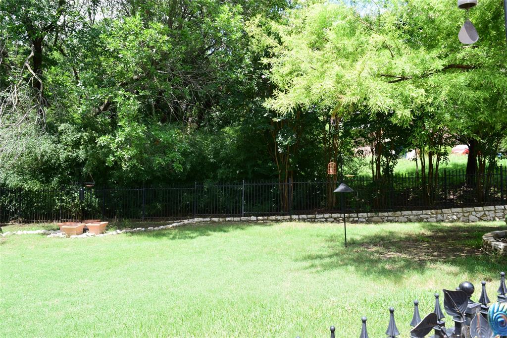 4201 Glistening Spring Rowlett, TX 75088 - Photo 29 of 33 Expansive lawn area featuring a black wrought iron fence, natural stone retaining wall, and mature trees providing ample shade