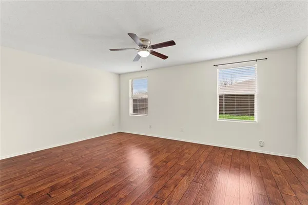 an empty room with wooden floor ceiling fan and windows
