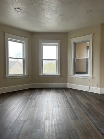 a view of an empty room with wooden floor and window