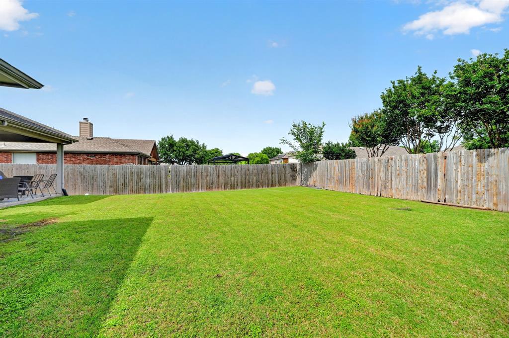 511 Chestnut Trail Forney, TX 75126 - Photo 30 of 32 Spacious backyard with a wood privacy fence, expansive green lawn, and mature perimeter trees